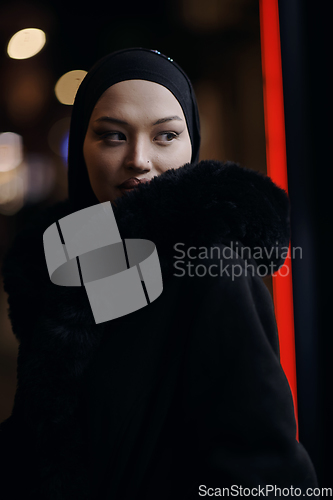 Image of Muslim woman walking on urban city street on a cold winter night wearing hijab