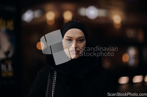 Image of Muslim woman walking on urban city street on a cold winter night wearing hijab