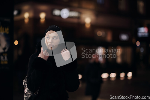 Image of Muslim woman walking on urban city street on a cold winter night wearing hijab