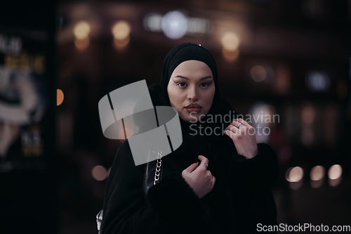 Image of Muslim woman walking on urban city street on a cold winter night wearing hijab