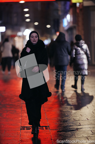 Image of Muslim woman walking on urban city street on a cold winter night wearing hijab