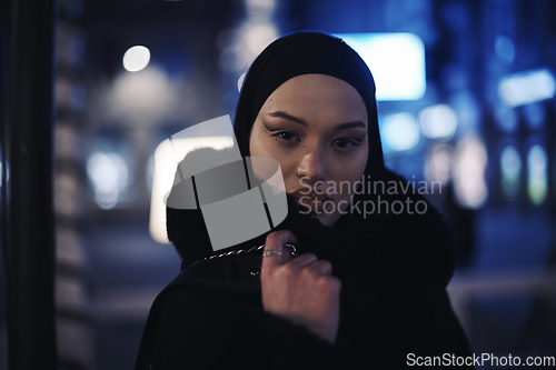 Image of Muslim woman walking on urban city street on a cold winter night wearing hijab