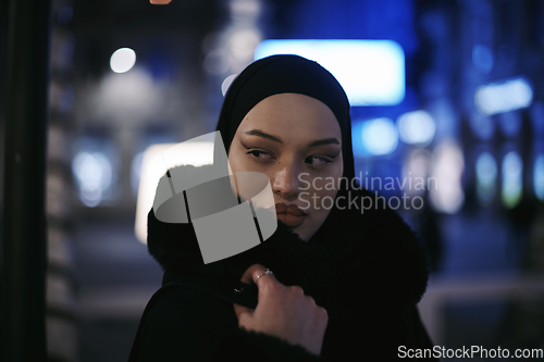 Image of Muslim woman walking on urban city street on a cold winter night wearing hijab