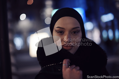 Image of Muslim woman walking on urban city street on a cold winter night wearing hijab