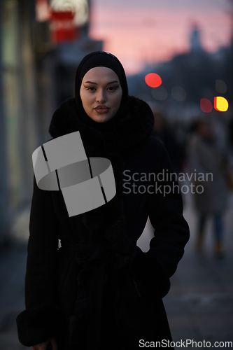 Image of Muslim woman walking on an urban city street on a cold winter night wearing hijab