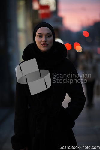 Image of Muslim woman walking on an urban city street on a cold winter night wearing hijab