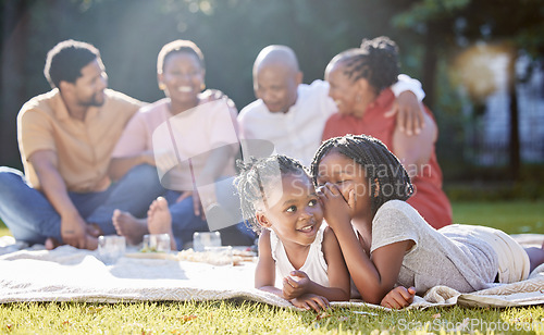 Image of Secret, sister and children with a girl whispering to her sibling and a black family in the background. Kids, mystery and gossip with a female child being secretive on a picnic in the park in summer