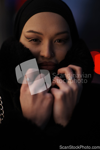 Image of Muslim woman walking on an urban city street on a cold winter night wearing hijab