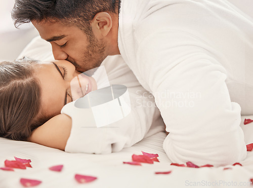 Image of Love, a kiss and rose petals, a couple in bed, happy and celebrating an engagement or honeymoon. Floral romance, marriage and a anniversary celebration of man and woman together on romantic holiday.