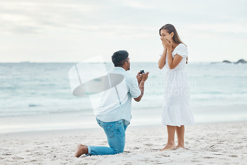 Image of Love, couple and beach engagement proposal for marriage, partnership and commitment on ocean sea sand. Wow, shocked and surprised woman with romantic man on one knee presenting a union wedding ring