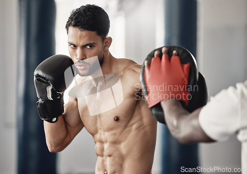 Image of Fitness, training and a man boxing in gym with personal trainer and sparring pads. Health, motivation and exercise, boxer throwing a punch. Fight, muscle and workout with sports gloves in mma studio.