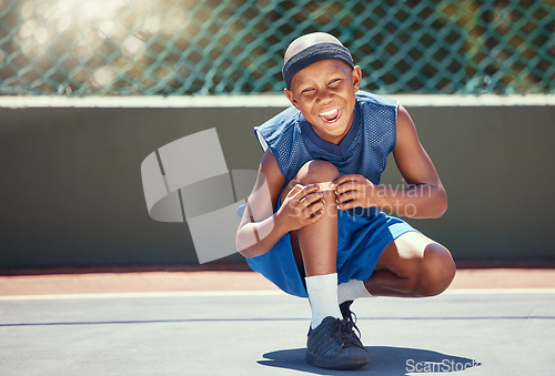 Image of Child with a band aid on a knee injury from sports outside on a basketball court touching his bandage. Boy with a medical plaster hurt by accident while training or practicing for a game.