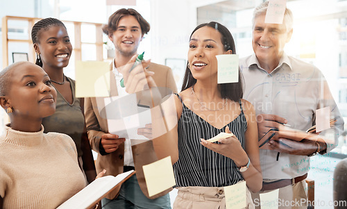 Image of Team of workers in office, brainstorming together and writing idea on sticky notes at glass board. Management teamwork, thinking and planning new strategy for company with goals on paper