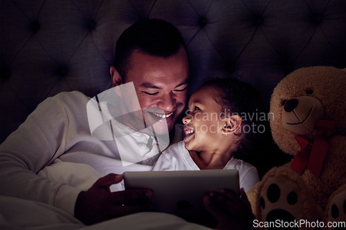 Image of Father and child in bed with tablet reading ebook or to watch a film together at night. Happy girl with her dad enjoying online live streaming movie, game or digital kid app in dark home bedroom