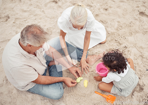 Image of Family, beach and play with grandparents and child building sand castle together for vacation, fun and relax. Summer, happy and retirement couple with young girl playing by the sea for holiday break