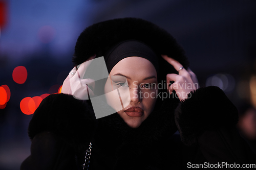 Image of Muslim woman walking on an urban city street on a cold winter night wearing hijab