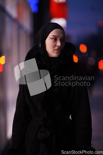 Image of Muslim woman walking on an urban city street on a cold winter night wearing hijab