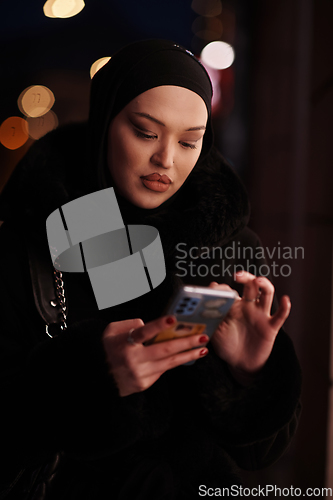 Image of uropean Muslim Hijabi Business Lady checking her phone on urban city street at night