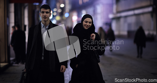 Image of Happy multicultural business couple walking together outdoors in an urban city street at night near a jewelry shopping store window.