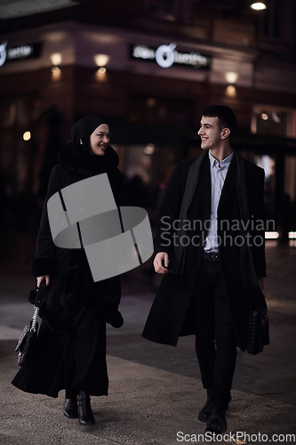 Image of Happy multicultural business couple walking together outdoors in an urban city street at night near a jewelry shopping store window.