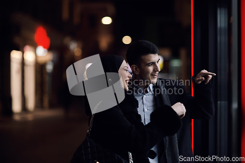 Image of Happy multicultural business couple walking together outdoors in an urban city street at night near a jewelry shopping store window.