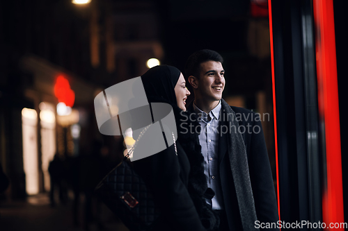 Image of Happy multicultural business couple walking together outdoors in an urban city street at night near a jewelry shopping store window.