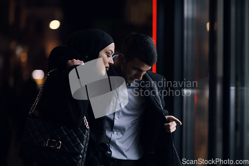 Image of Happy multicultural business couple walking together outdoors in an urban city street at night near a jewelry shopping store window.