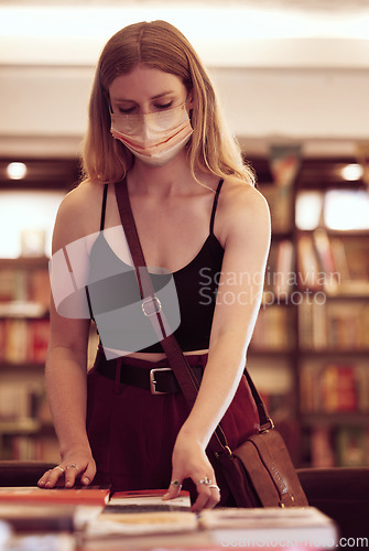 Image of Covid, face mask and woman with books in a library, bookshop or educational building for knowledge, reading or research. Young female student browsing and choosing novel on table in a bookstore