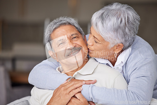 Image of Happy Mexico senior couple kiss on living room sofa for love, care and trust in romantic relationship at house or home. Elderly people or retirement man and woman smile, hug and kissing face cheek