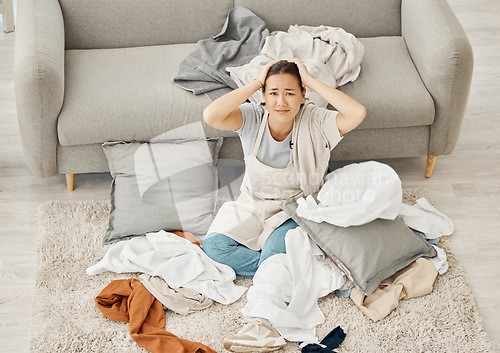 Image of Laundry chaos, cleaning stress and woman tired with anxiety on living room floor, confused burnout and sad in lounge of apartment with clothes. Portrait of service cleaner with mess problem in home