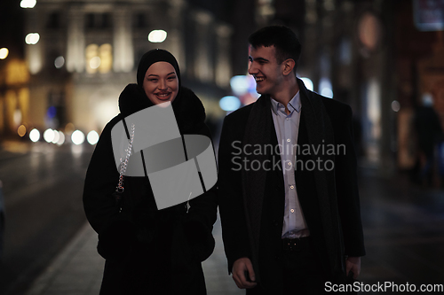 Image of Happy multicultural business couple walking together outdoors in an urban city street at night near a jewelry shopping store window.