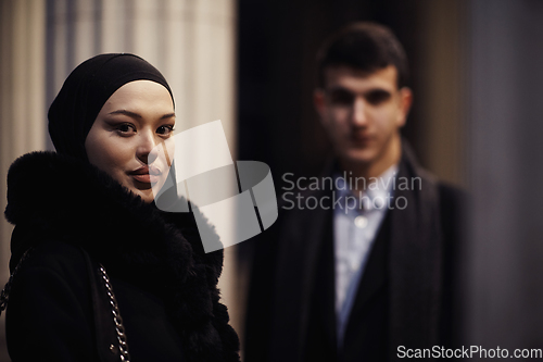 Image of Happy multicultural business couple walking together outdoors in an urban city street at night near a jewelry shopping store window.