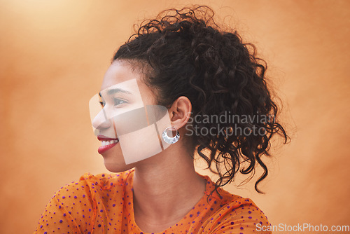 Image of Face, beauty and hair with a woman in studio against an orange background while posing with a smile from the side. Fashion, happy and idea with a young female standing on a bright color wall indoor