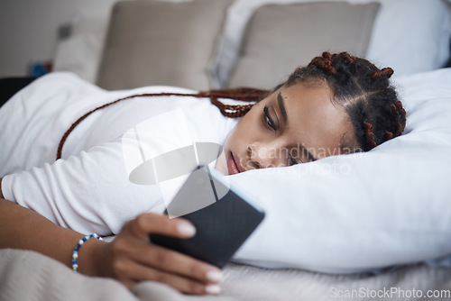 Image of Depression, sad and african woman on a phone relaxing on the bed in her bedroom at home. Tired, mental health and lonely black girl browsing on social media or internet while having breakup problems.