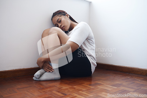 Image of Depression, anxiety and lonely woman sitting in a corner suffering from mental health issues or problems. Black female in stress, depressed or abuse alone on a wooden floor in apartment, home or room