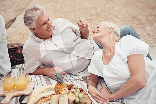 Image of Food, beach and picnic senior couple dating or on romantic honeymoon date with fruit, snack and drink. Happy, love and romance woman and man or elderly people eating and feed together for anniversary