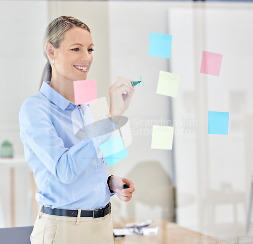 Image of Writing, planning and thinking with sticky notes on a glass in a modern office. Happy woman manager, leader or ceo plan strategy on post it paper in a corporate marketing and advertising company