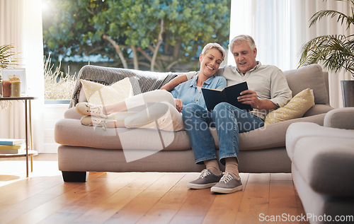 Image of Retirement senior couple with photo album book on sofa together in summer house for vacation holiday. Happy elderly woman or people relax on couch in living room reading, talking of marriage history