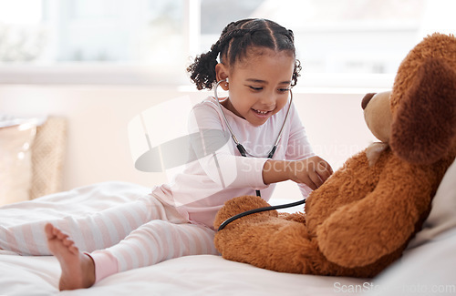 Image of A black girl playing hospital doctor with a teddy bear on her bed, holding a stethoscope and imagining a kid. Child development for a future job as a physician, clinic nurse and medical professional