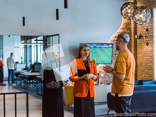 Image of A group of young business colleagues, including a woman in a hijab, stands united in the modern corridor of a spacious startup coworking center, representing diversity and collaborative spirit