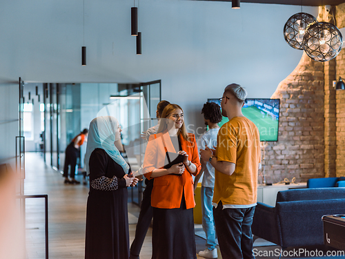 Image of A group of young business colleagues, including a woman in a hijab, stands united in the modern corridor of a spacious startup coworking center, representing diversity and collaborative spirit