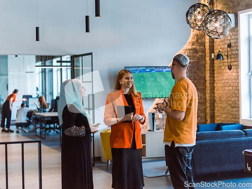 Image of A group of young business colleagues, including a woman in a hijab, stands united in the modern corridor of a spacious startup coworking center, representing diversity and collaborative spirit