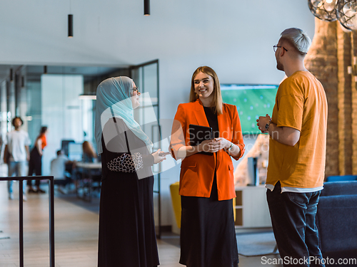 Image of A group of young business colleagues, including a woman in a hijab, stands united in the modern corridor of a spacious startup coworking center, representing diversity and collaborative spirit