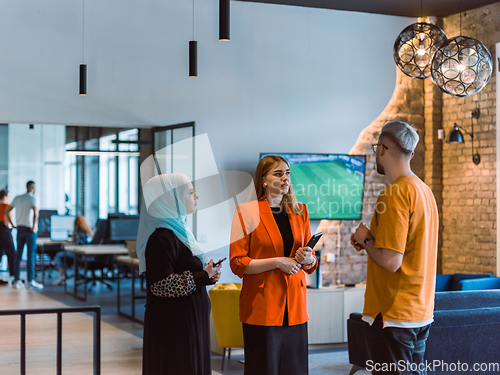 Image of A group of young business colleagues, including a woman in a hijab, stands united in the modern corridor of a spacious startup coworking center, representing diversity and collaborative spirit