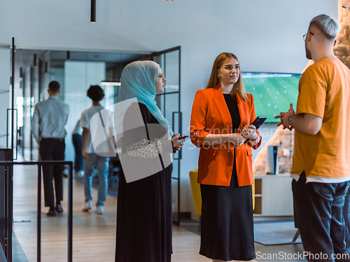 Image of A group of young business colleagues, including a woman in a hijab, stands united in the modern corridor of a spacious startup coworking center, representing diversity and collaborative spirit