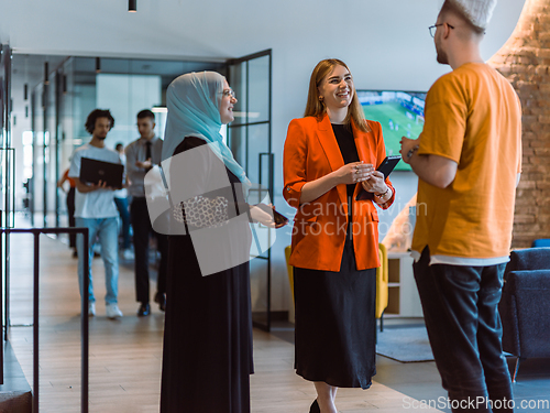 Image of A group of young business colleagues, including a woman in a hijab, stands united in the modern corridor of a spacious startup coworking center, representing diversity and collaborative spirit