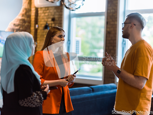 Image of A group of young business colleagues, including a woman in a hijab, stands united in the modern corridor of a spacious startup coworking center, representing diversity and collaborative spirit