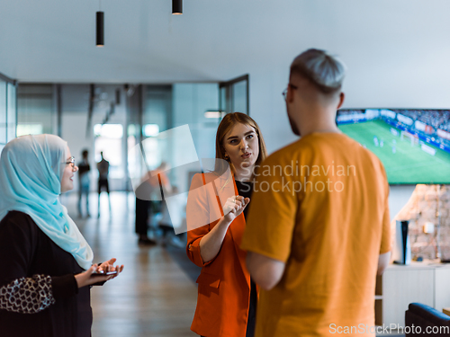 Image of A group of young business colleagues, including a woman in a hijab, stands united in the modern corridor of a spacious startup coworking center, representing diversity and collaborative spirit