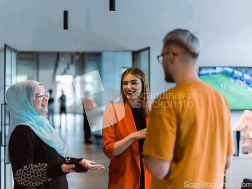 Image of A group of young business colleagues, including a woman in a hijab, stands united in the modern corridor of a spacious startup coworking center, representing diversity and collaborative spirit