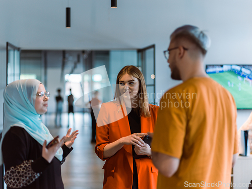 Image of A group of young business colleagues, including a woman in a hijab, stands united in the modern corridor of a spacious startup coworking center, representing diversity and collaborative spirit